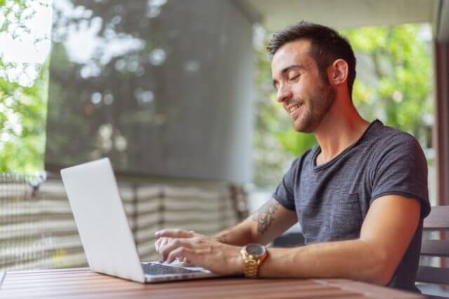 man typing on laptop sitting in enclosed porch