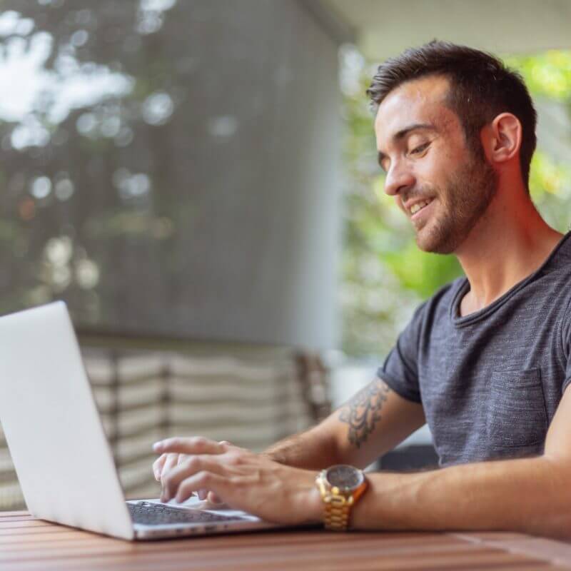 man typing on laptop sitting in enclosed porch